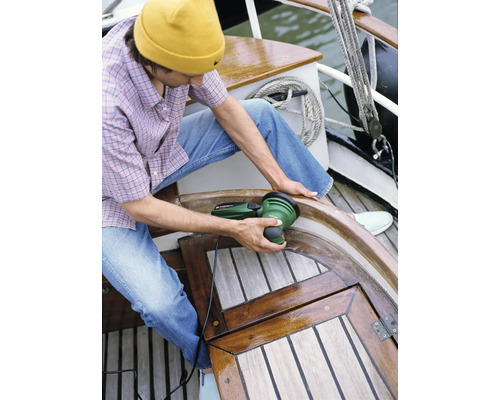 Eine Person verwendet einen Exzenterschleifer auf einem Holzboot.