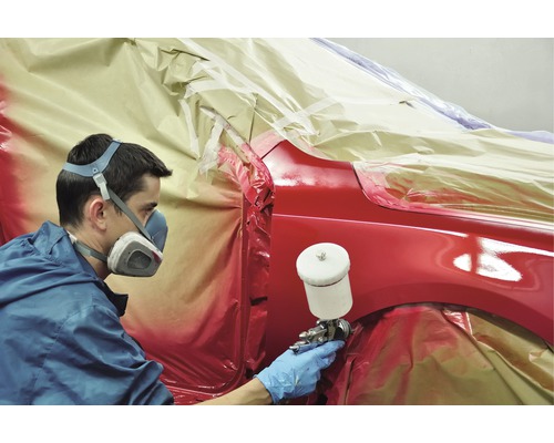 Peintre automobile au travail avec un pistolet de pulvérisation et un masque de protection.