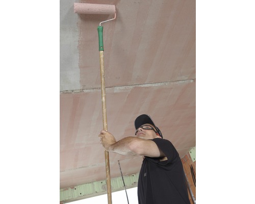 Un homme peint le plafond d''une pièce avec un rouleau à peinture sur un bâton