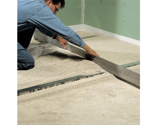 Handwerker nivelliert Trockenschüttung mit einer Richtlatte auf dem Boden.