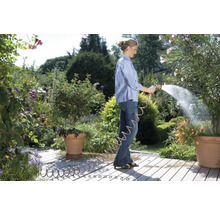 Femme arrose des plantes avec un tuyau d''arrosage dans le jardin.