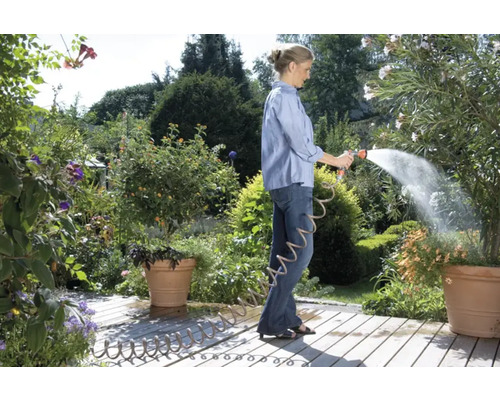 Femme arrose des plantes avec un tuyau d''arrosage dans le jardin.