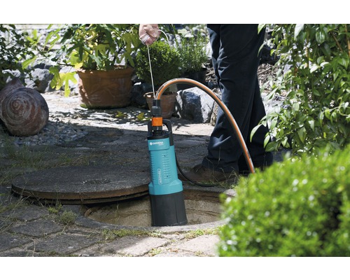 Garten-Schmutzwasserpumpe im Einsatz neben einem Kanaldeckel im Garten.
