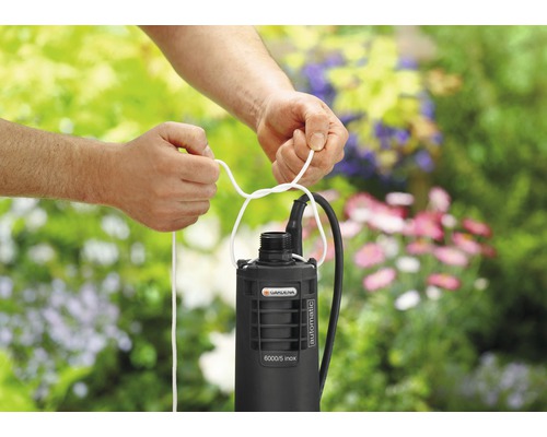 Gartenpumpe mit befestigtem Seil vor einem Blumenhintergrund