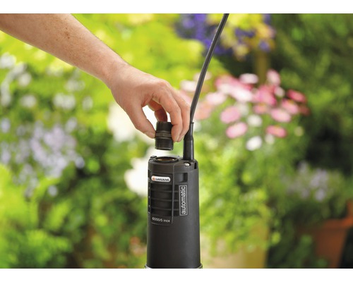 Gartenpumpe mit Hand beim Anbringen eines Anschlussstücks im Garten