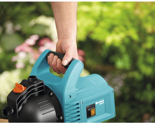 Gardena Hauswasserwerk 3000/4 mit Tragegriff in der Hand vor Gartenkulisse