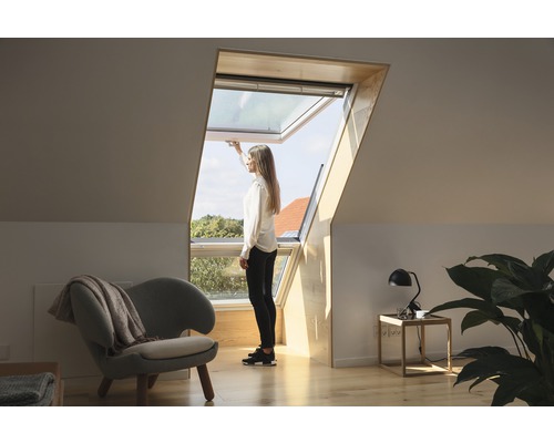 Frau öffnet ein Dachfenster in einem hellen Dachgeschosszimmer.