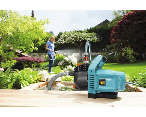 Garten mit Gartenpumpe und Frau, die mit einem Schlauch gießt