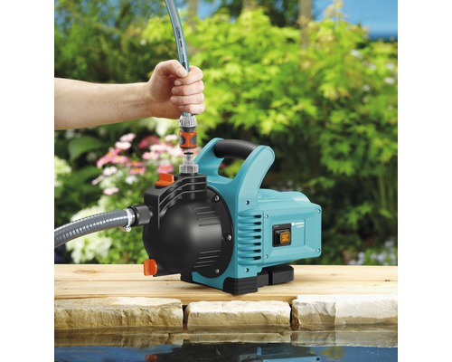 Gartenpumpe auf einem Holzsteg neben einem Teich mit einer Person, die einen Schlauch anschliesst