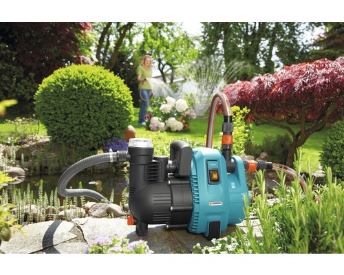 Garten mit Teich und einer Frau, die mit einer Gardena Gartenpumpe Blumen bewässert