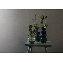 Szene mit grauer Textiltapete und einem Arrangement aus grünen Glasvasen mit Blumen auf einem kleinen Tisch
