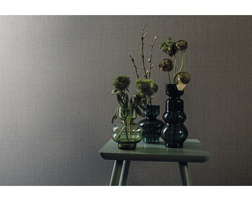 Scène avec papier peint textile gris et arrangement de vases en verre verts avec des fleurs sur une petite table