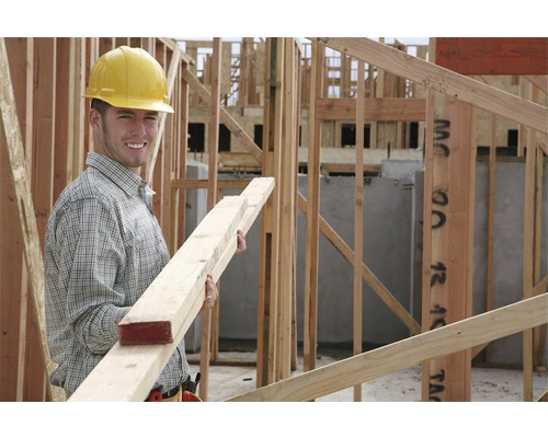 Un ouvrier du bâtiment avec un casque de protection tient des lattes en bois sur un chantier.