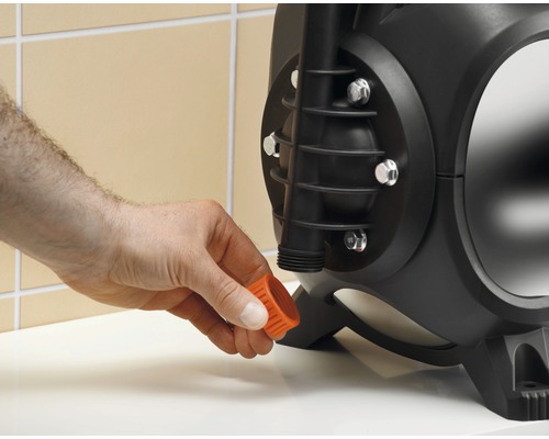 Une pompe de jardin noire avec un bouchon orange est actionnée par une main.