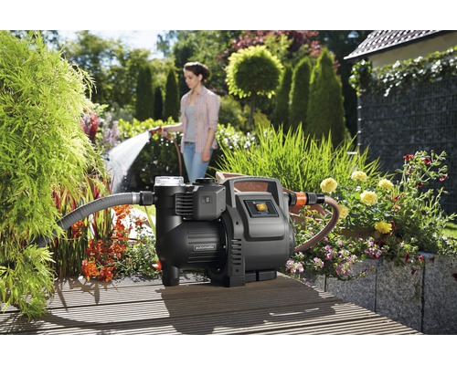 Hauswasserwerk im Garten mit gießender Frau im Hintergrund