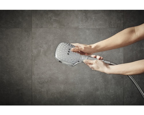Brausekopf mit Brauseschlauch in Händen vor Wandfliesen