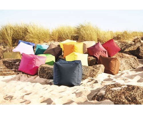 Un ensemble de coussins carrés de différentes couleurs sur du sable et des rochers.