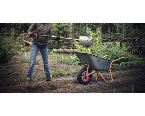 Eine Person befüllt eine Schubkarre im Garten mit einer Schaufel.