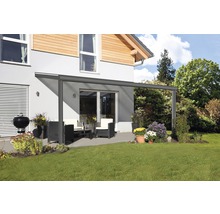 Terrassenüberdachung mit Gartenmöbeln und Grill auf einer Rasenfläche vor einem Haus