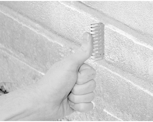 Une personne tient un rail métallique contre un mur de pierre