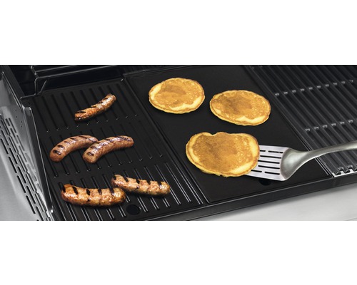 Grill mit Würstchen und Pfannkuchen auf einer Grillplatte mit einem Pfannenwender