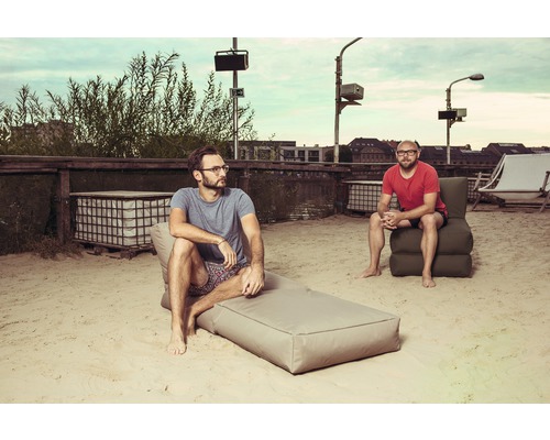 Zwei Männer entspannen auf einer Sandfläche mit Lounge-Möbeln.