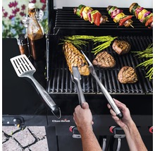 Personne faisant griller des steaks, des asperges et des brochettes de légumes sur un barbecue avec des ustensiles de grillade et des sauces