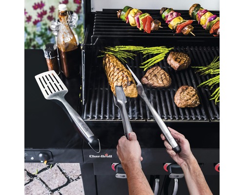 Person grillt Steaks, Spargel und Gemüsespieße auf einem Grill mit Grillbesteck und Saucen