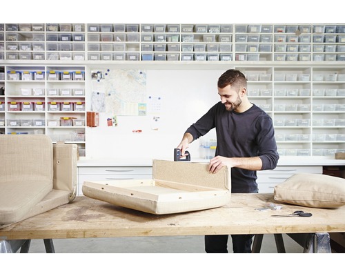 Un homme utilise une agrafeuse pour rembourrer un meuble dans un atelier.