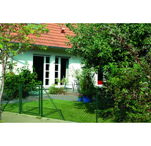 Ein grüner Maschendrahtzaun mit Tor umgibt einen Garten vor einem Haus.
