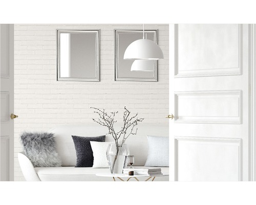 Salon lumineux avec canapé, coussins, table, décoration, lampes, miroirs et porte ouverte.