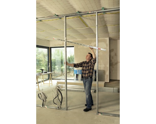 Mann montiert Trockenbauwand mit Metallprofilen und Messwerkzeug in einem Raum.