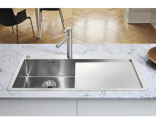 Évier en acier inoxydable avec égouttoir et robinetterie sur un plan de travail en marbre.