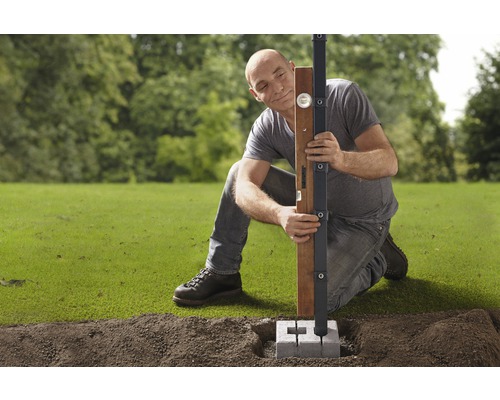 Mann richt Holzpfosten mit Wasserwaage und Pfostenträger im Garten aus.