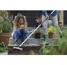 Scène de jardinage avec une femme préparant le sol avec un râteau, tandis qu''un enfant regarde