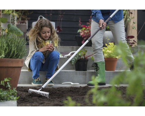 Scène de jardinage avec une femme préparant le sol avec un râteau, tandis qu''un enfant regarde