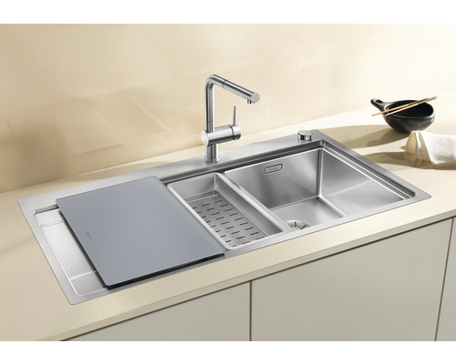 Edelstahlspüle mit Schneidebrett, Abtropfschale und Küchenarmatur auf einer Küchentheke.