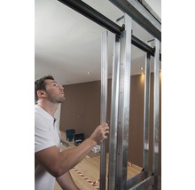 Un homme installe une structure de porte coulissante faite de profilés métalliques dans une pièce.