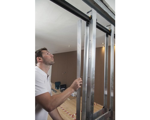 Un homme installe une structure de porte coulissante faite de profilés métalliques dans une pièce.