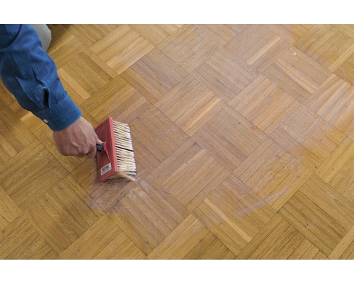 Une personne applique une substance sur un parquet avec un pinceau.