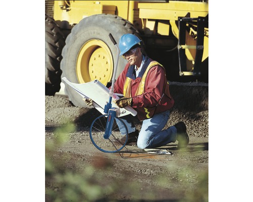 Ein Arbeiter mit Bauplan und Messrad vor einem Bagger.