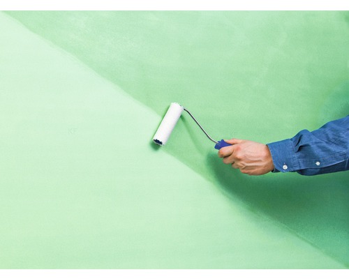 Ein Mann streicht eine Wand mit einer Farbrolle. Die Wand ist teilweise gestrichen.