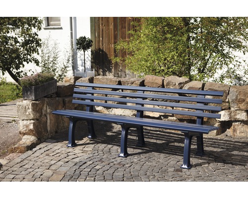 Banc de jardin en métal devant un mur de pierres et des pavés
