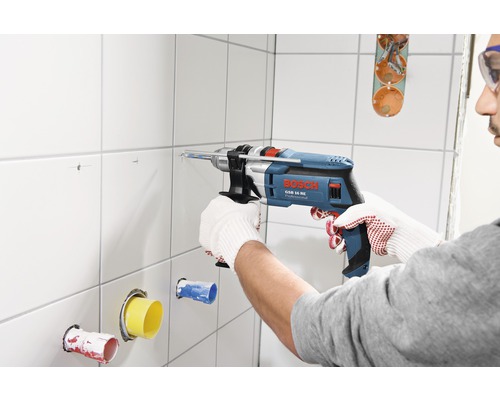 Handwerker bohrt mit einer Bosch Schlagbohrmaschine GSB 16 RE Professional in eine geflieste Wand.