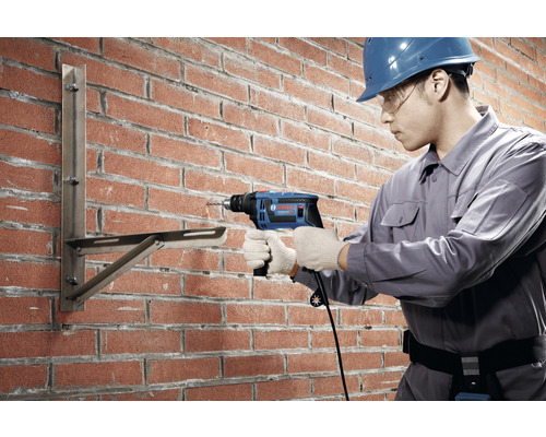 Handwerker bohrt mit einer Bohrmaschine ein Loch in eine Ziegelwand, um eine Halterung zu befestigen.