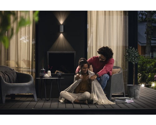 Un couple est assis sur une terrasse avec des luminaires extérieurs, des chaises, une table et des décorations.