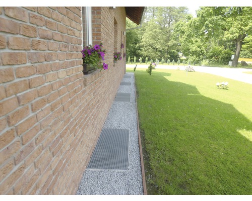 Außenansicht eines Hauses mit Ziegelmauer, Kiesweg und Metallgitterrosten vor Fenstern