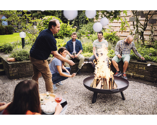 Gruppe von Personen, die Marshmallows über einer Feuerschale im Garten rösten