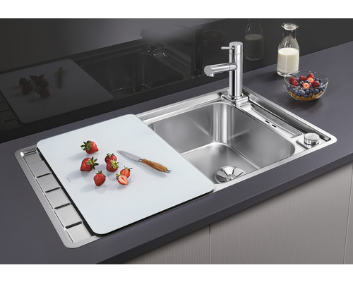 Spüle aus Edelstahl mit Schneidebrett, Armatur und frischen Früchten