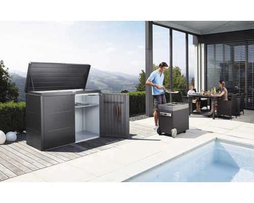 Gartenszene mit Gerätehaus, Grill und Familie am Esstisch auf der Terrasse